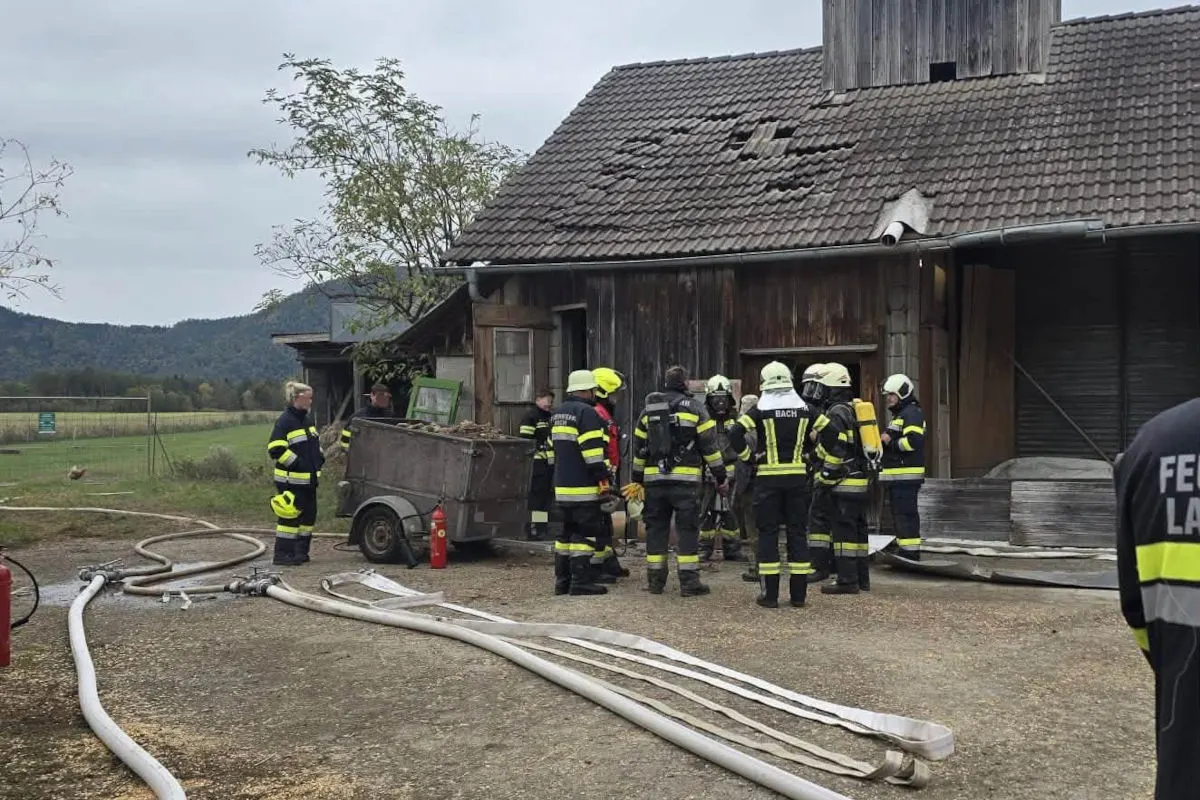 Feuerwehrleute stehen vor einem Gebäude mit beschädigtem Dach und führen Inspektionen durch. Im Vordergrund liegen Schläuche und Ausrüstung.