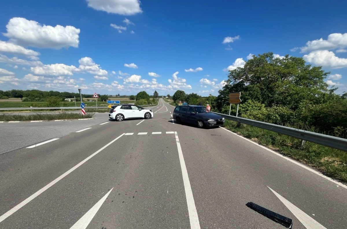 Zwei Autos, ein weißes und ein schwarzes, blockieren die Straße an einer Kreuzung. Ein sonniger Tag mit blauem Himmel und weißen Wolken.