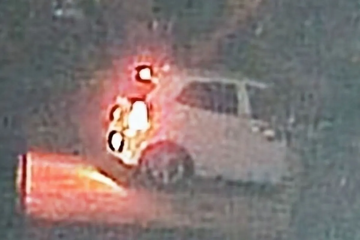 Ein weißes Auto, das bei Nacht in Flammen steht. Das Feuer leuchtet hell und ist der Blickfang des Bildes.