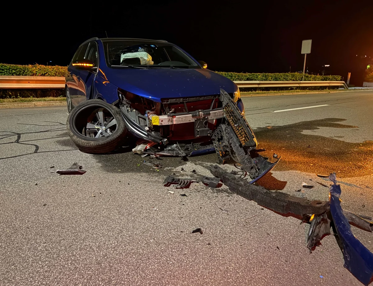 Ein stark beschädigtes blaues Auto steht nach einem Unfall bei Nacht auf einer Straße. Die Vorderachse liegt herausgerissen daneben.