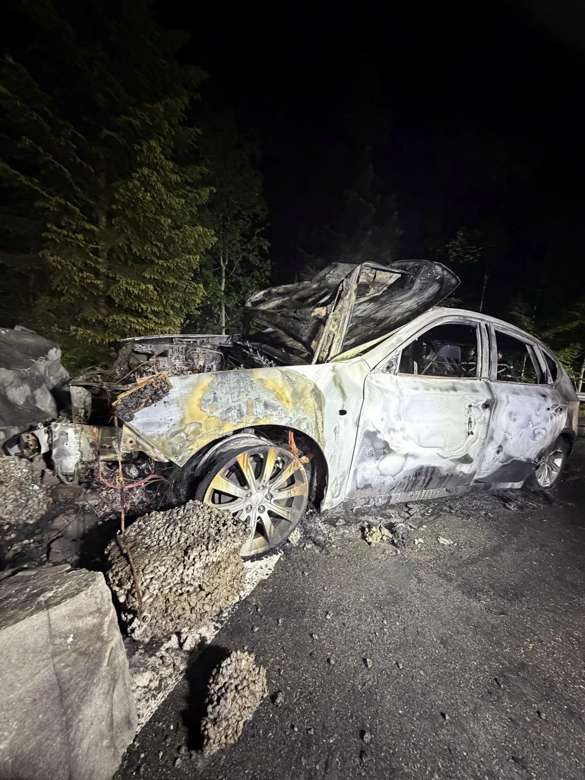 Ein ausgebrannter Pkw mit schweren Schäden steht auf einer Straße. Der Vorderteil ist stark zerstört, umgeben von Trümmern.