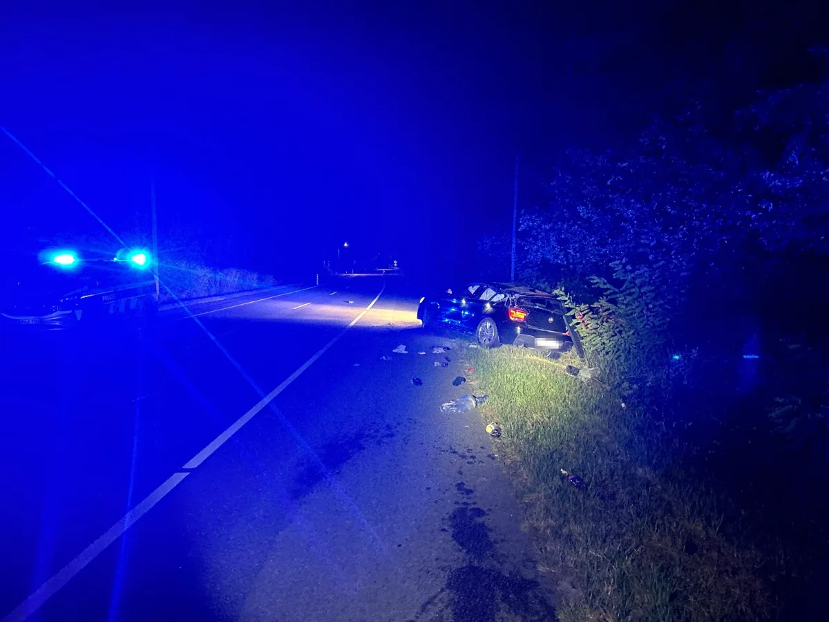 Ein Fahrzeug ist von der Fahrbahn abgekommen und steht beschädigt am Straßenrand. Blaulichter eines Polizeiwagens sind ebenfalls zu sehen.