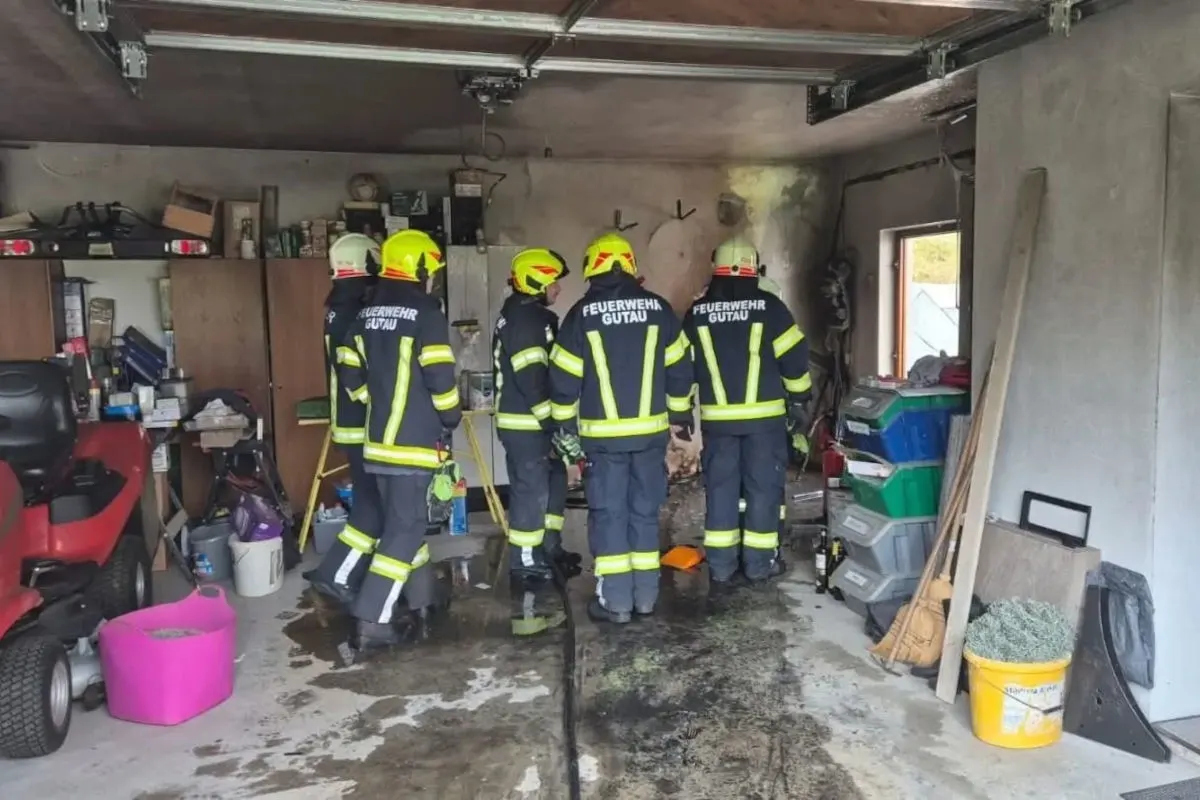 Fünf Feuerwehrleute der Feuerwehr Gutau stehen in einer Garage mit verrußten Wänden, umgeben von Werkzeugen und Gegenständen.
