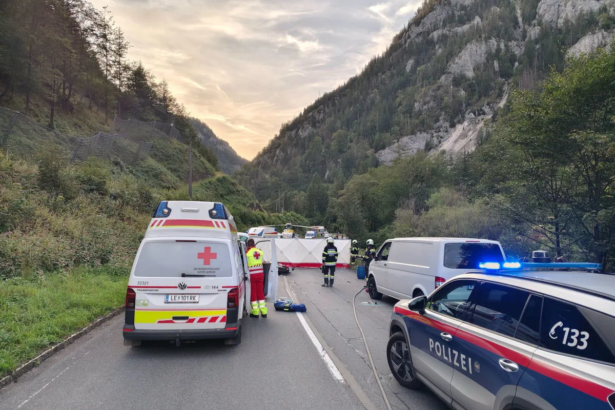 Eine alpine Bergstraße ist gesperrt, Rettungskräfte und notfallfahrzeuge sind im Einsatz. Polizeiautos und ein Rettungswagen stehen auf der Straße, während Einsatzkräfte sichtbar sind.