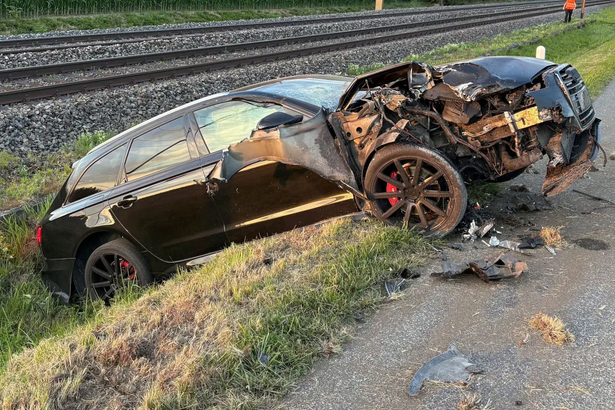 Ein schwarzes Auto mit schweren Frontschäden liegt nahe Bahngleisen im Graben. Trümmerteile sind verstreut.