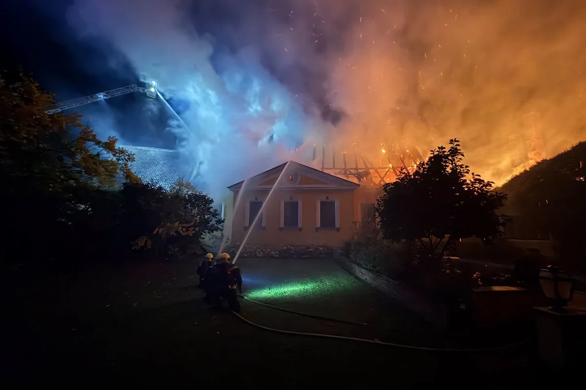Mehrere Feuerwehrleute bekämpfen nachts einen intensiven Hausbrand. Flammen und dichter Rauch sind sichtbar.