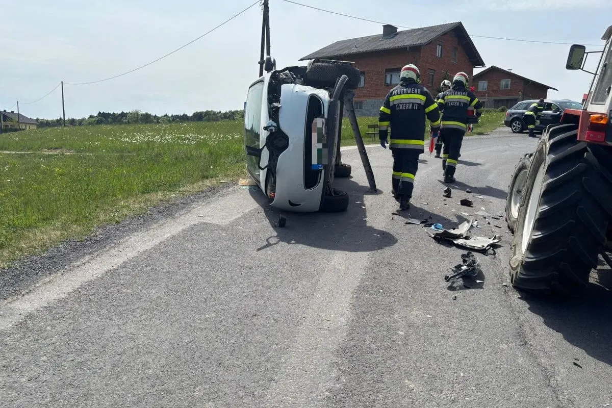 Ein Auto liegt auf der Seite auf einer Landstraße. Feuerwehrleute in Uniformen sind anwesend und begutachten die Unfallstelle neben einem Traktor.