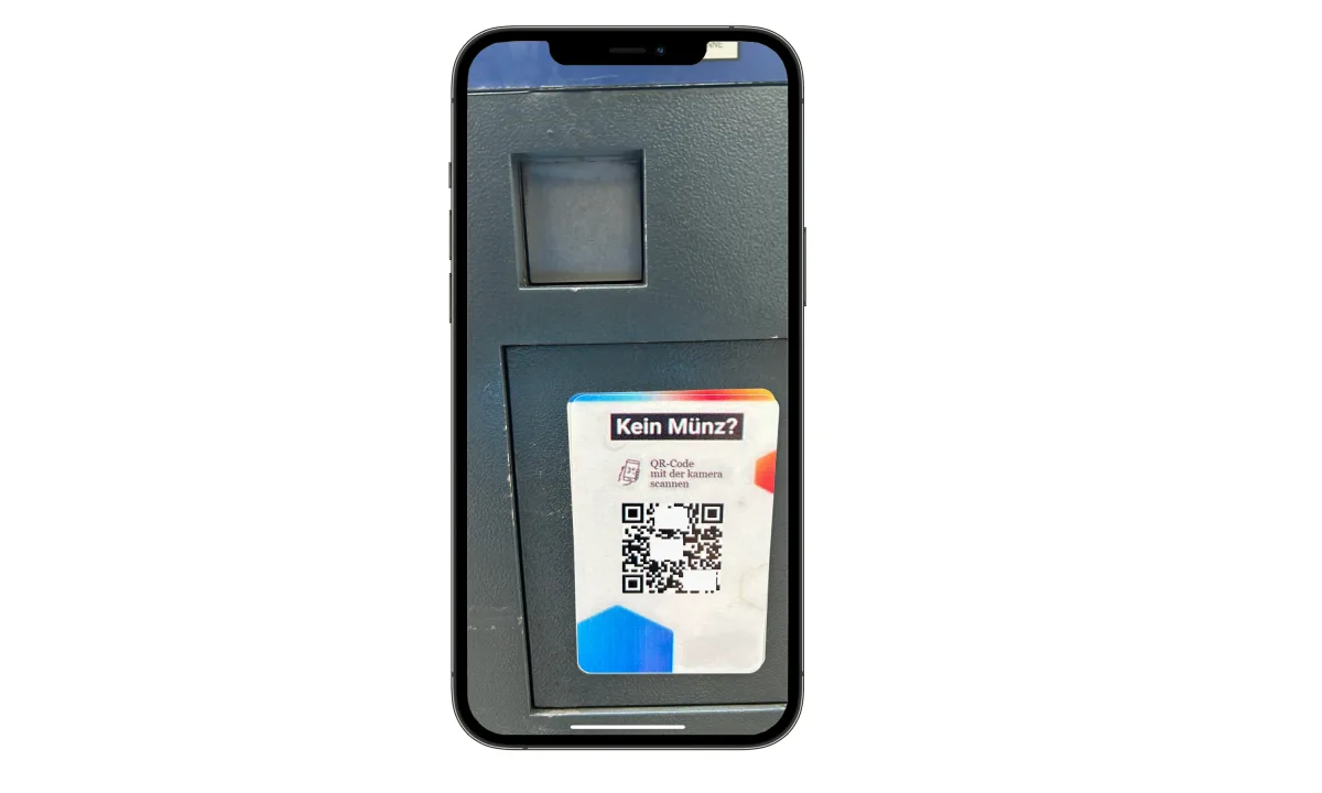 Ein Parkautomat mit einem QR-Code-Aufkleber für bargeldloses Bezahlen ist zu sehen. Der Aufkleber trägt die Aufschrift 'Kein Münz?'.