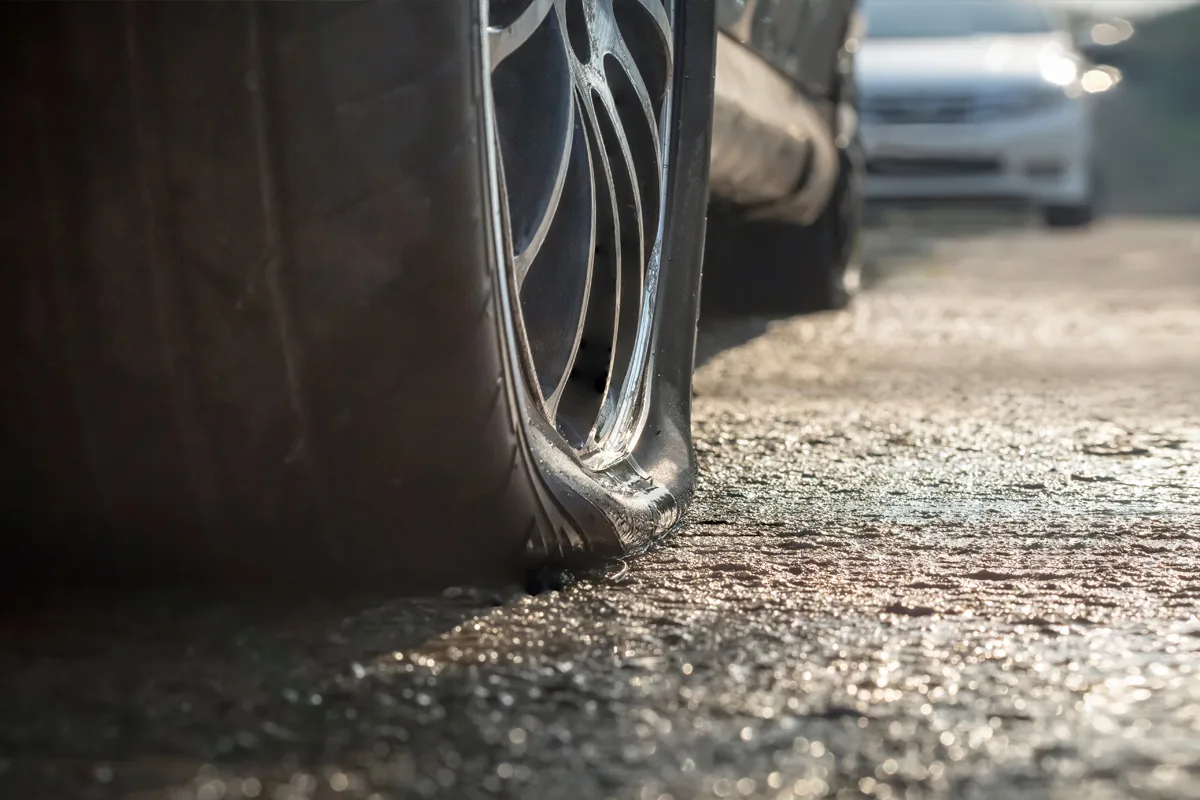 Ein platter Autoreifen ist in Nahaufnahme auf trockenem Asphalt zu sehen, mit einem leicht unscharfen Auto im Hintergrund.