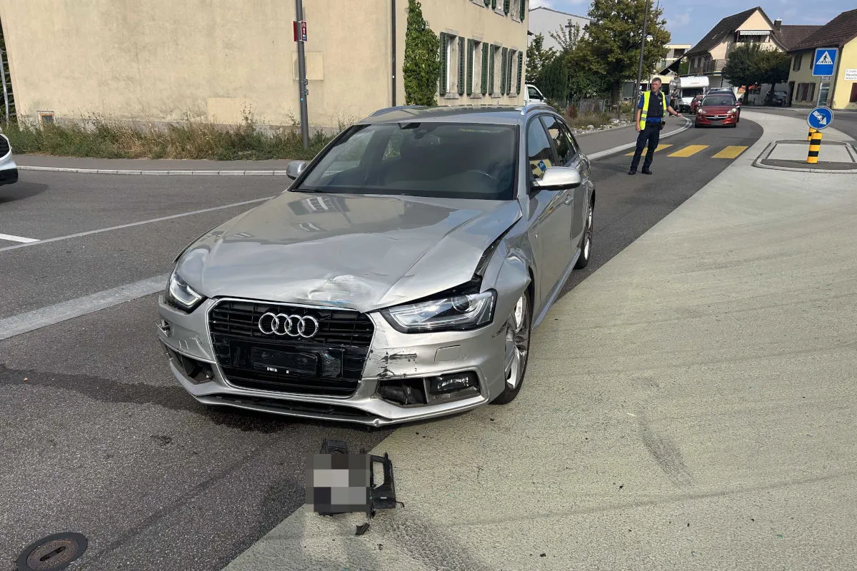 Ein beschädigter silberner Audi steht auf einer Straße. Ein Polizist ist im Hintergrund zu sehen.
