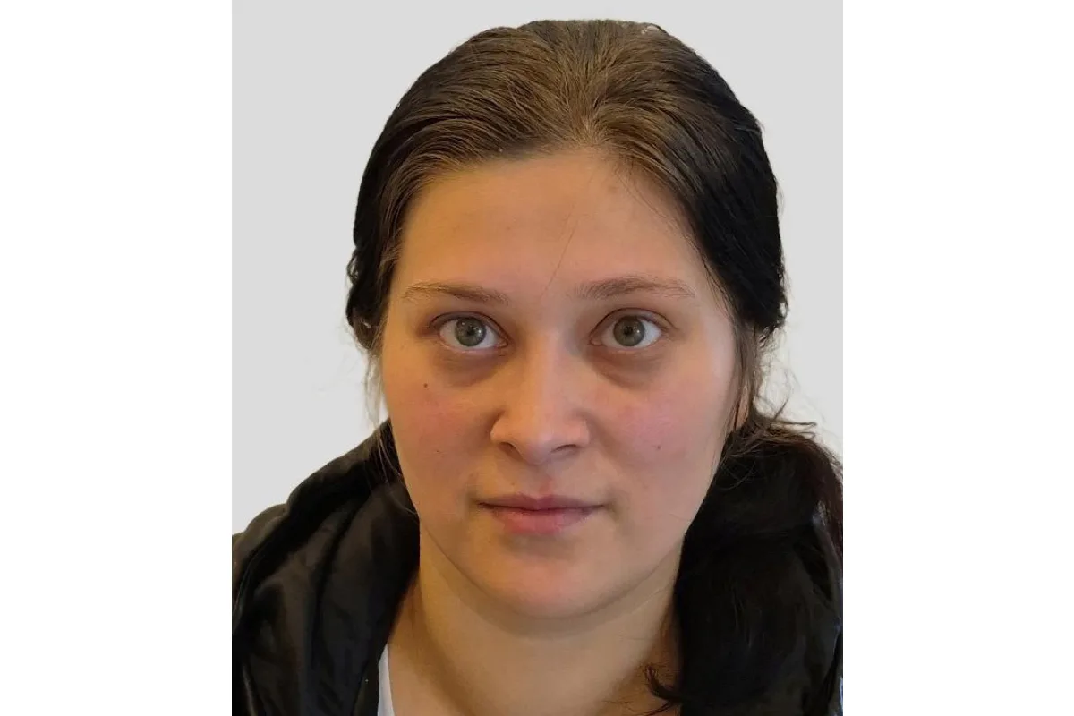Nahaufnahmefoto einer Frau mit langen dunklen Haaren und neutralem Gesichtsausdruck vor einem einfarbigen Hintergrund.