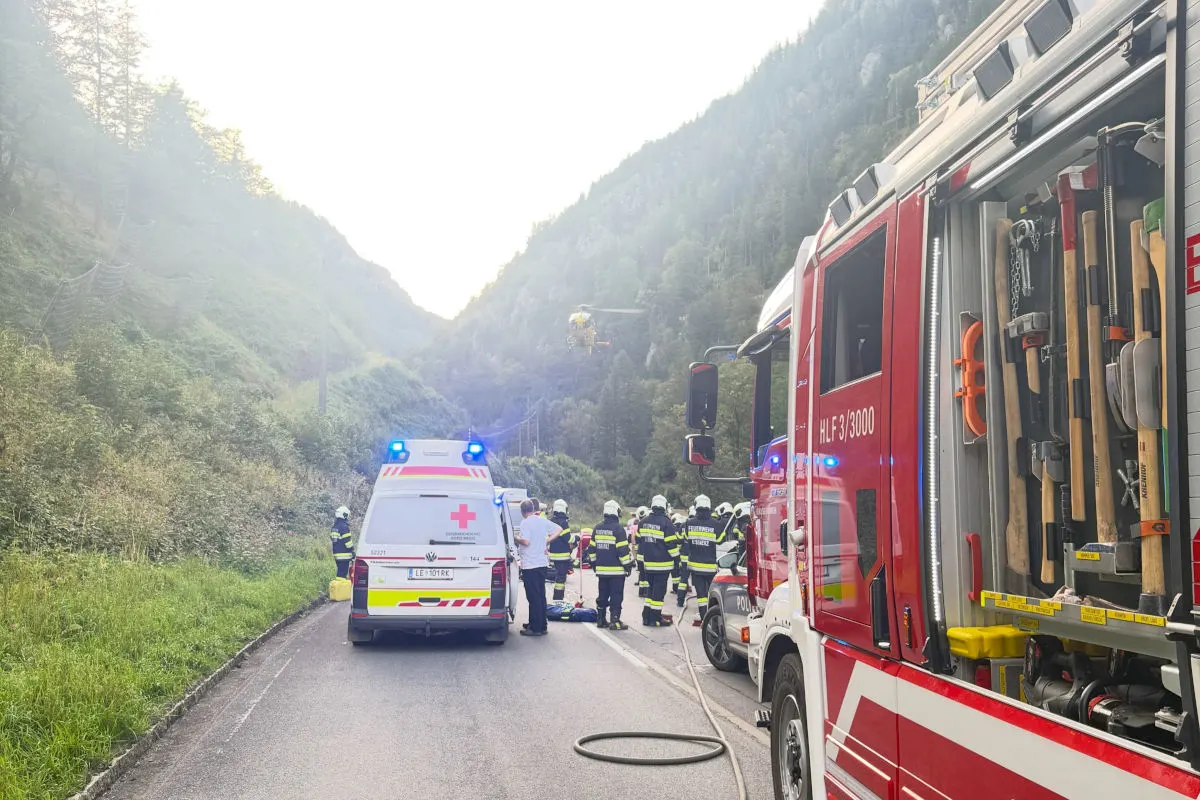 Ein Feuerwehrfahrzeug und ein Rettungswagen sind auf einer Straße in einem alpinen Tal im Einsatz. Im Hintergrund helfen Einsatzkräfte.