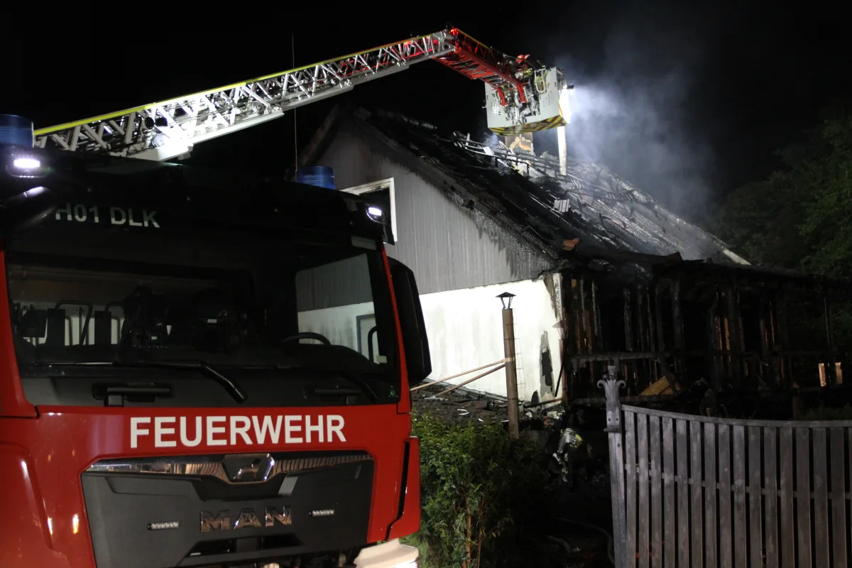 Ein Feuerwehrfahrzeug steht vor einem Haus, dessen Dach bei Nacht von einem Brand beschädigt wurde.