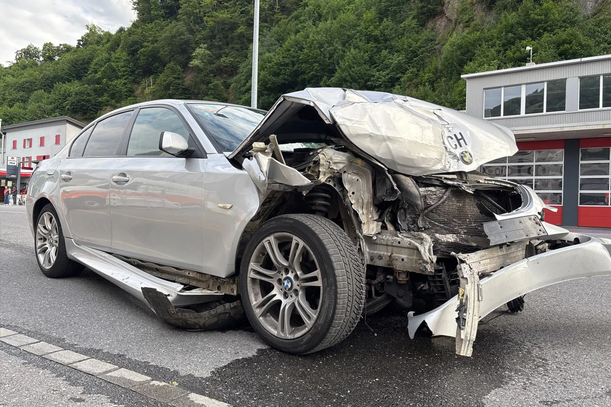 Ein silberner BMW steht mit stark beschädigter Frontpartie auf einer Straße. Im Hintergrund ist ein Gebäude zu sehen.