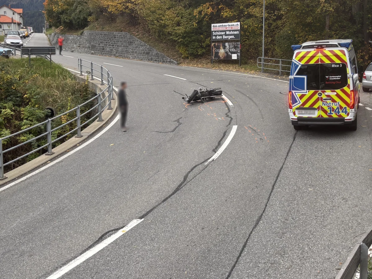 Ein umgefallenes Motorrad liegt auf einer kurvenreichen Straße in den Alpen, während ein Rettungswagen daneben steht.