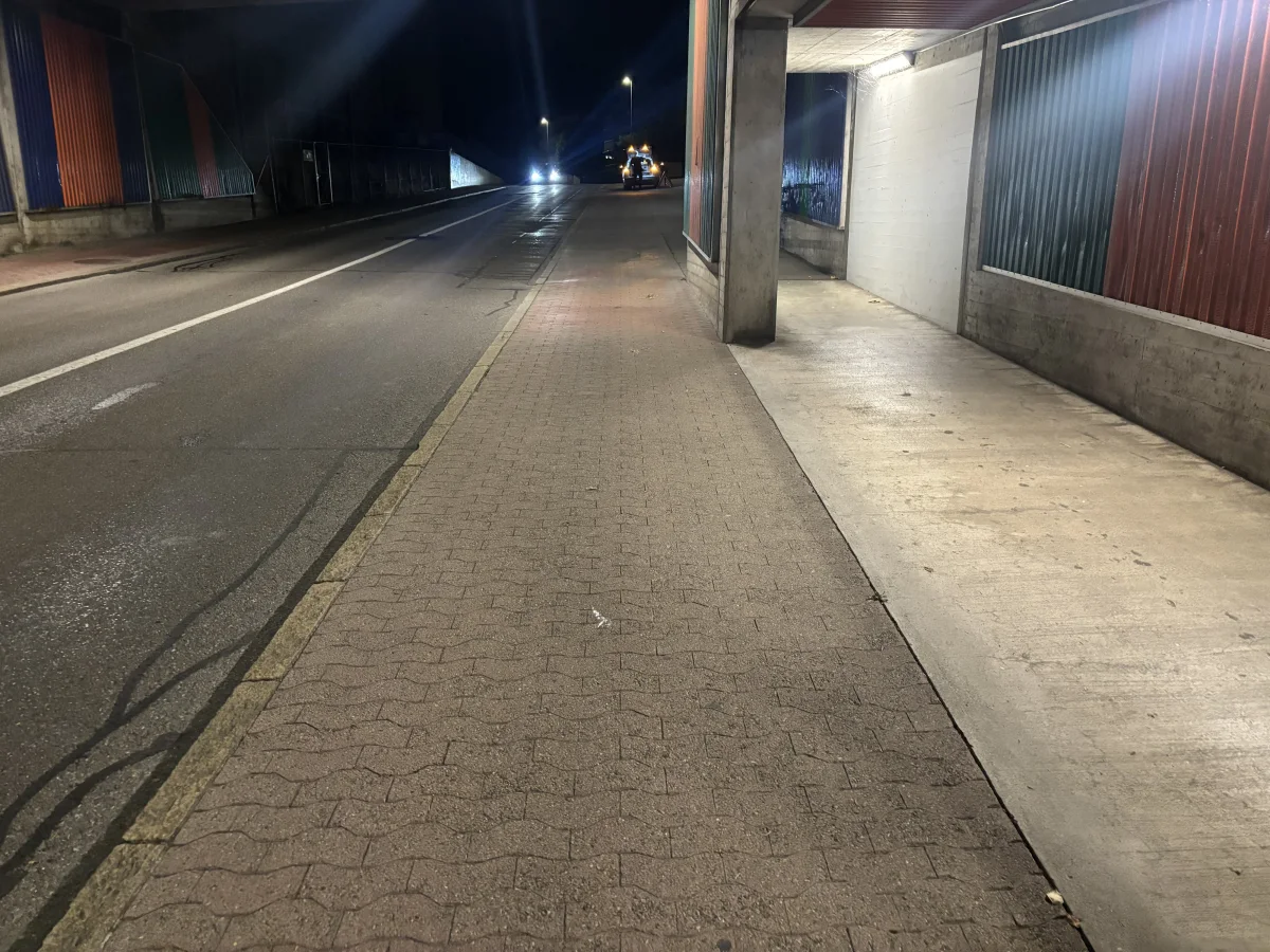 Eine nächtliche Straßenszene zeigt ein Auto, das mit eingeschaltetem Licht eine wenig beleuchtete Unterführung passiert.