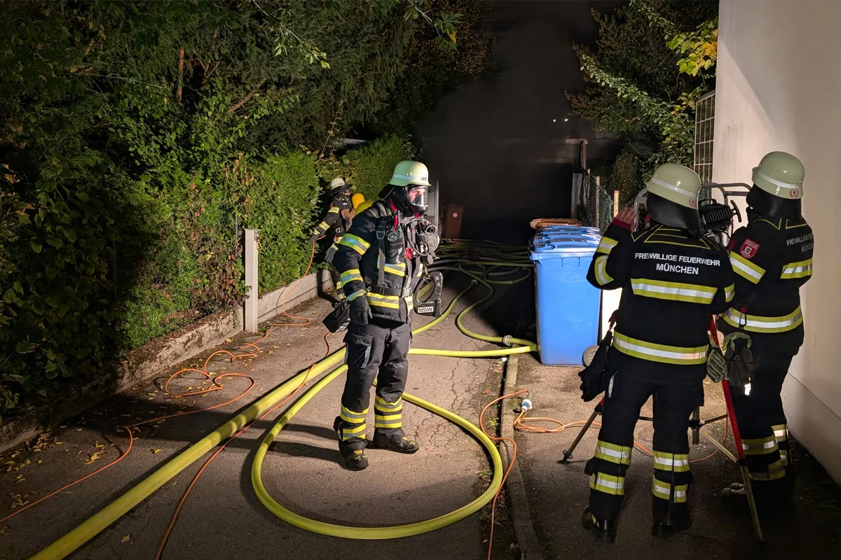 Mehrere Feuerwehrleute in voller Ausrüstung arbeiten nachts an einem Brand, Schläuche liegen am Boden.