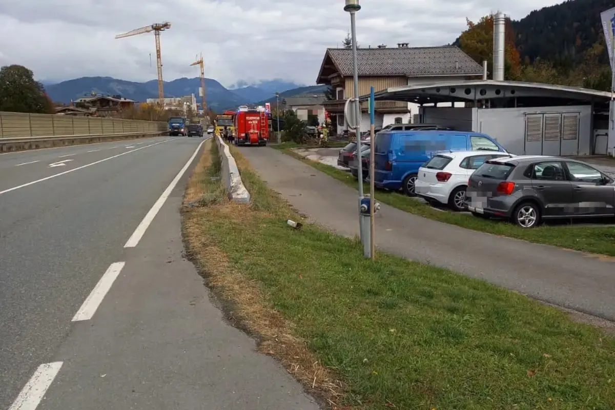 Ein rotes Feuerwehrfahrzeug steht auf einer Landstraße. Daneben sind mehrere parkende Fahrzeuge und Gebäude zu sehen.