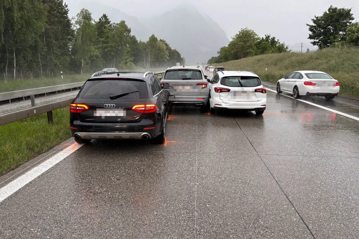 Mehrere Autos stehen nach einem Unfall auf einer nassen Autobahn. Es regnet und die Fahrzeuge haben sichtbare Schäden.
