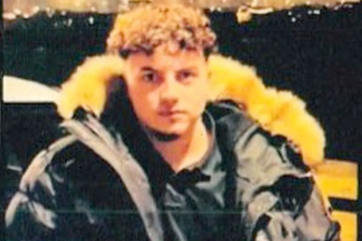 Ein junger Mann mit lockigem Haar, der eine schwarze Jacke mit einer auffälligen Fellkapuze trägt, sitzt frontal im Bild.
