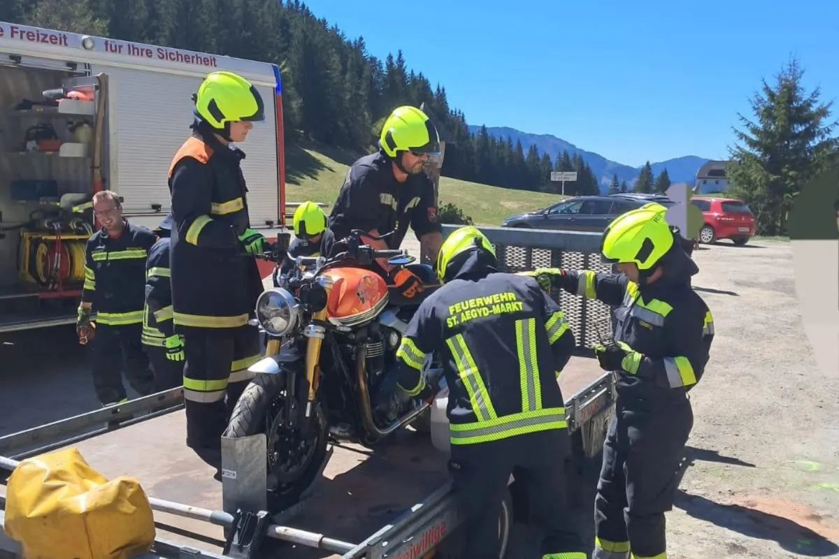 Mehrere Feuerwehrleute in Schutzkleidung sichern ein Motorrad auf einem Anhänger. Im Hintergrund steht ein Feuerwehrfahrzeug.