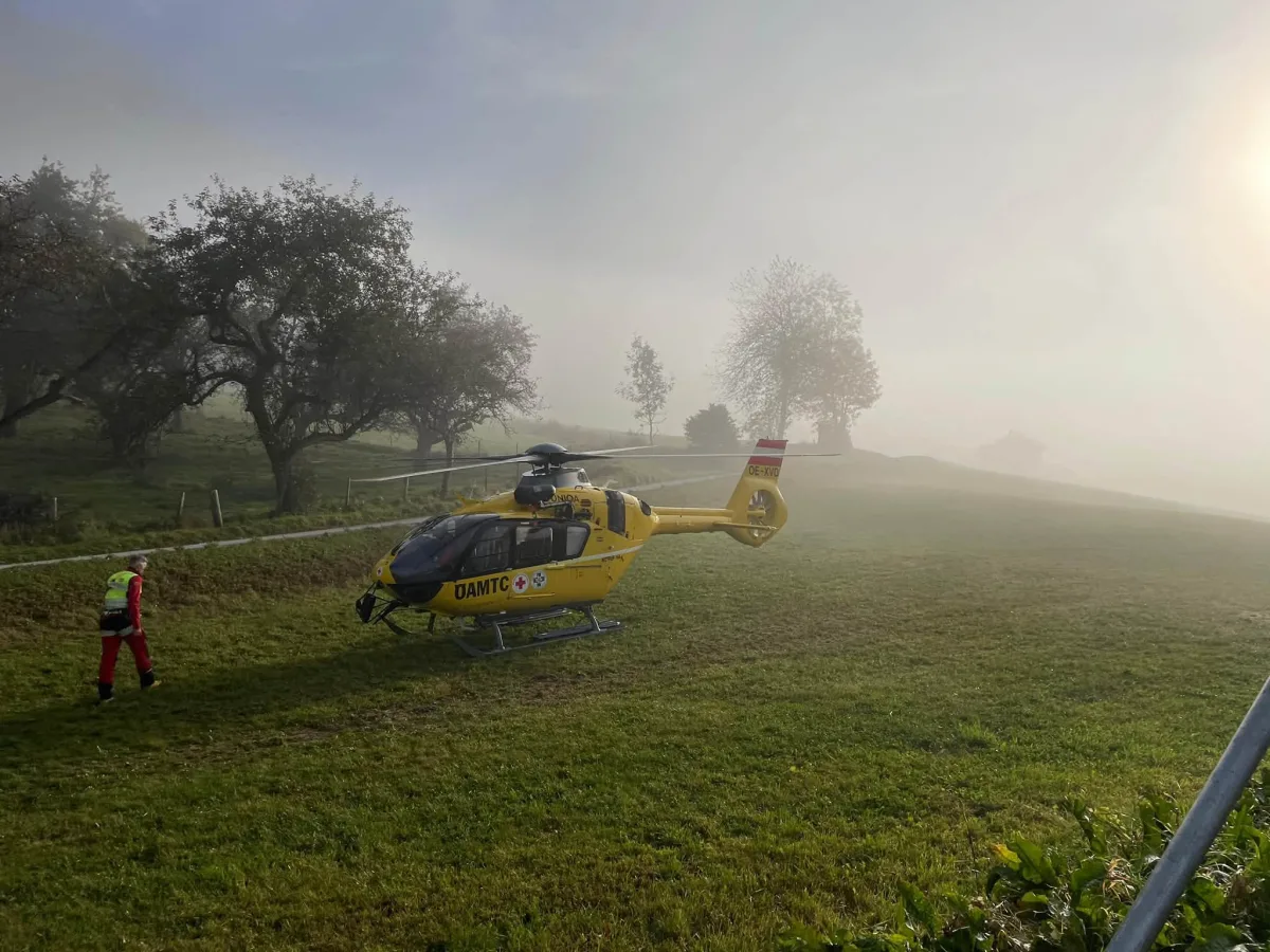 Ein gelber Rettungshubschrauber steht auf einer Wiese, während Nebel die Umgebung umhüllt. Ein Rettungssanitäter nähert sich dem Hubschrauber.