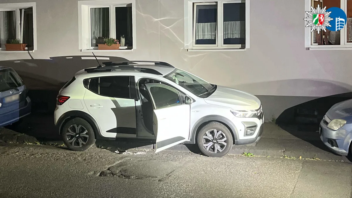 Ein weißer SUV steht vor einem Wohngebäude, die Fahrertür ist offen. Beleuchtung deutet auf polizeiliche Untersuchung hin.