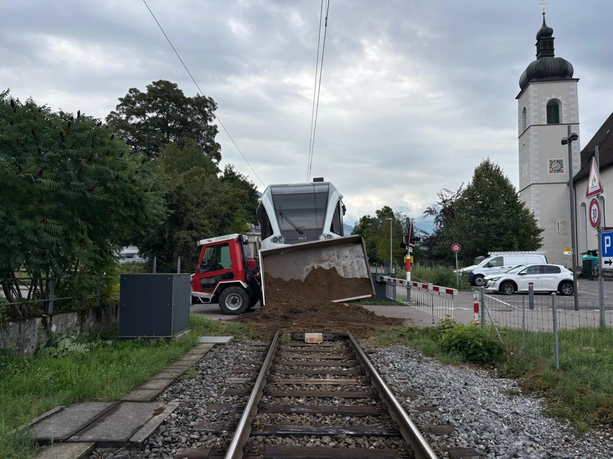 Ein entgleister Zug hat eine Ladung Schutt vor einem Bahnübergang verloren. Im Hintergrund ist eine Kirche sichtbar.
