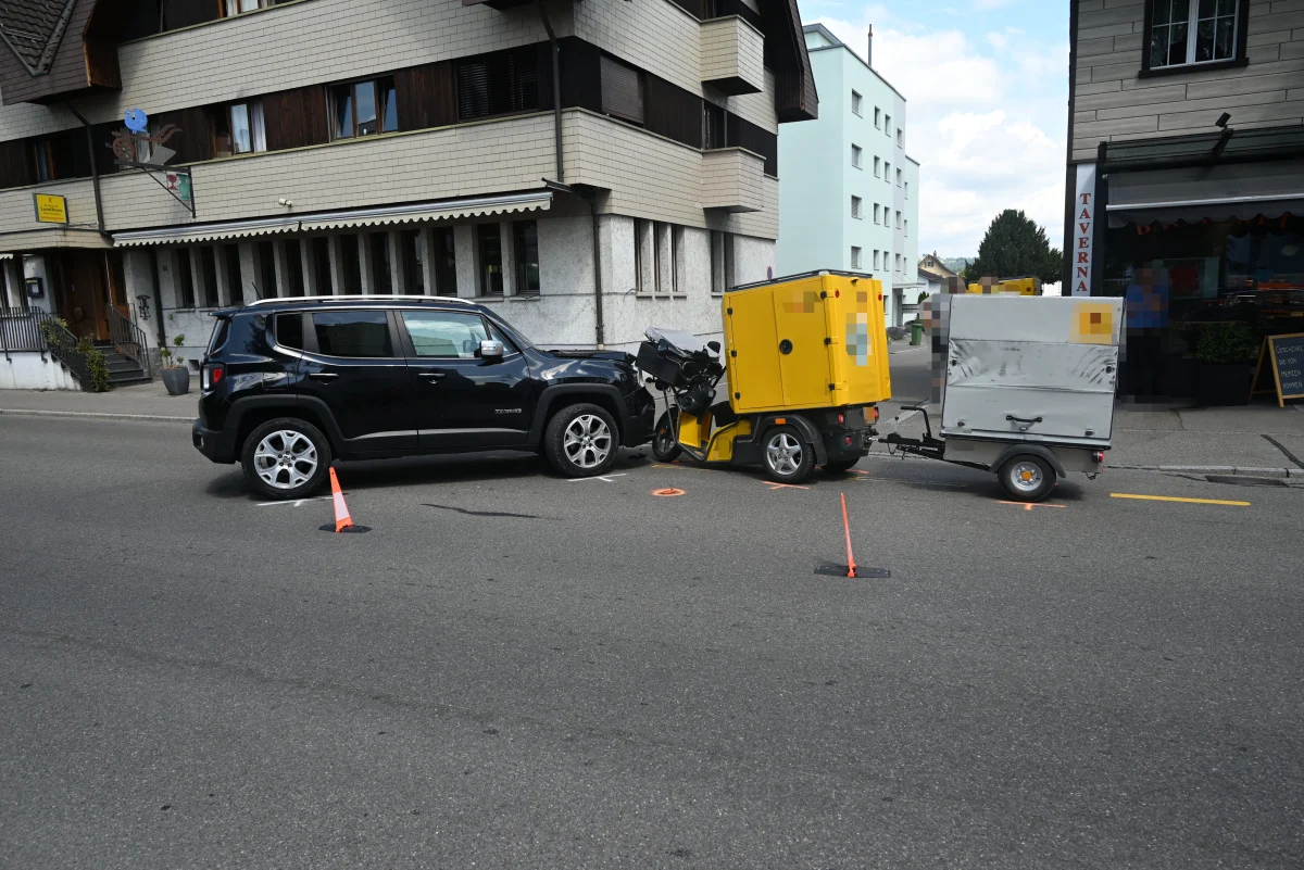 Ein schwarzer SUV ist auf einer Straße zu sehen, direkt dahinter steht ein gelber mobiler Anhänger. Die Szene spielt sich in einer städtischen Umgebung ab.