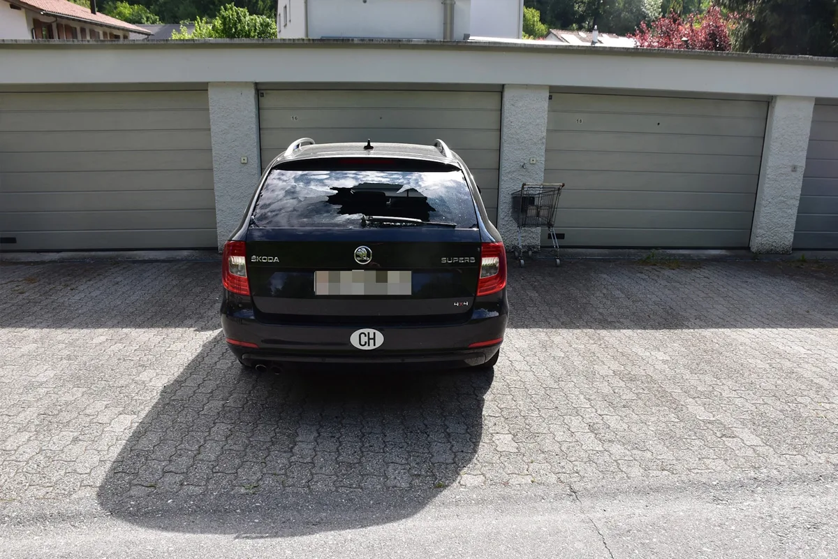 Ein schwarzer Skoda Kombi steht vor einer Garagenanlage. Die Heckscheibe des Fahrzeugs ist zerbrochen, ein Einkaufswagen steht daneben.