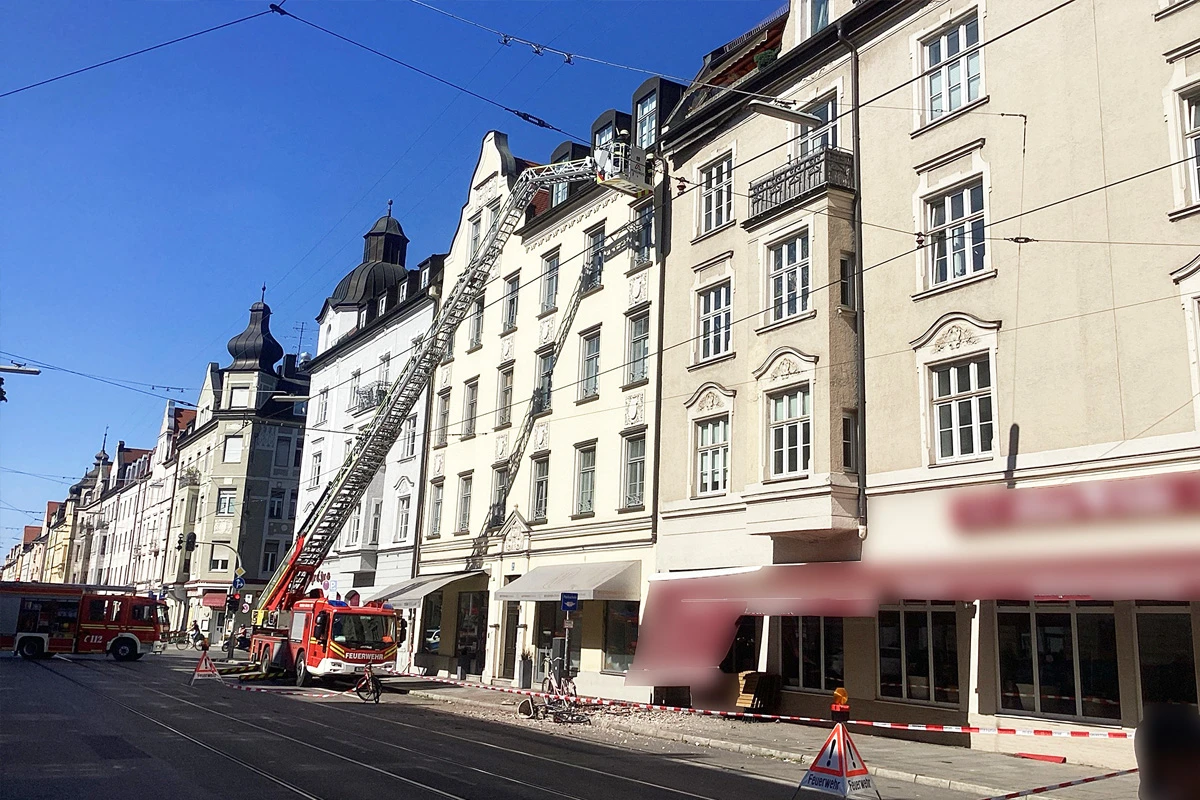 Eine Feuerwehrleiter ist an einem mehrstöckigen, historischen Gebäude in einer Stadtszene ausgefahren. Es sind mehrere Feuerwehrfahrzeuge zu sehen.