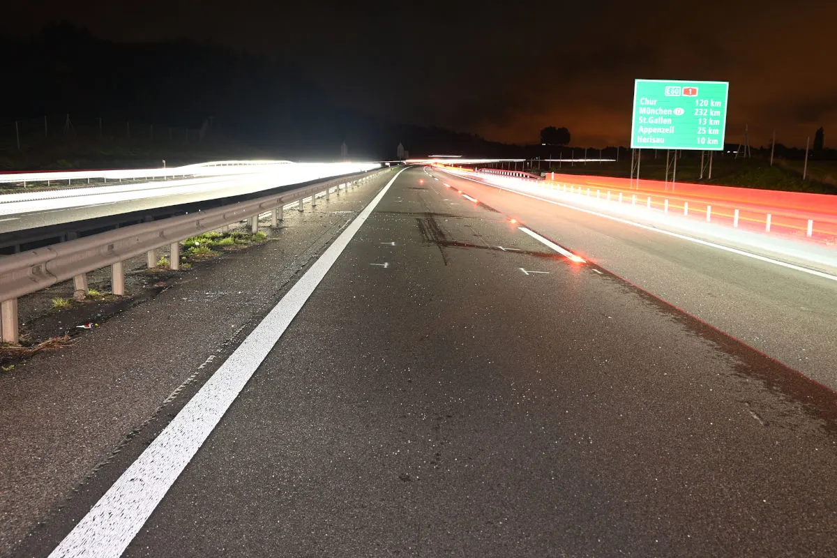 Die nächtliche Aufnahme zeigt eine leere Autobahn mit Lichtspuren der Fahrzeuge. Ein grünes Autobahnschild gibt Entfernungen an.