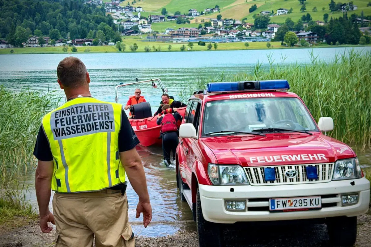 Ein Feuerwehrfahrzeug und ein Einsatzleiter am Ufer eines Sees, während Feuerwehrleute ein Boot aufs Wasser bringen.