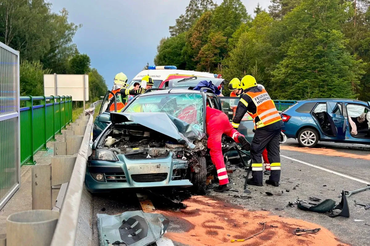 Ein schwer beschädigtes Auto mit Einsatzkräften, die einen Fahrer bergen. Im Hintergrund ist ein Rettungswagen sichtbar.