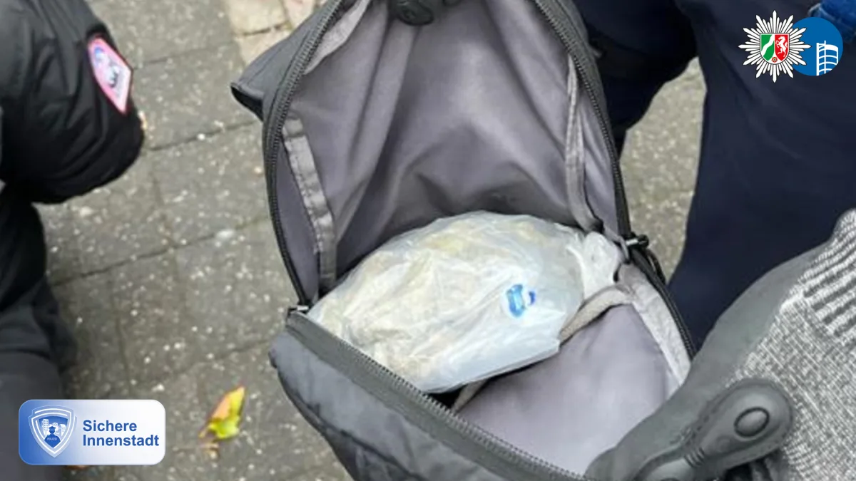 Auf einem Bürgersteig wird eine geöffnete Tasche mit einem durchsichtigen Plastikbeutel darin gezeigt, daneben steht eine Person.