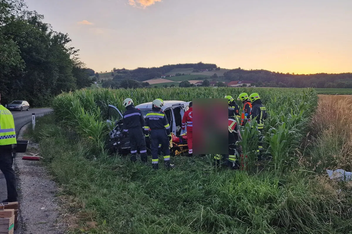 Ein Auto steht verunglückt in einem Feld, umgeben von Rettungskräften, die bei Sonnenuntergang Hilfe leisten.