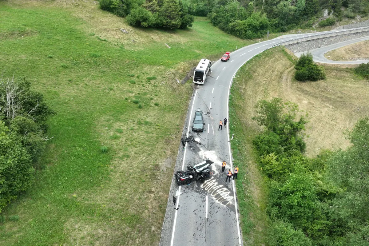 Eine kurvige Landstraße, auf der ein umgestürzter Bus und mehrere beschädigte Autos zu sehen sind. Einsatzkräfte sind vor Ort.