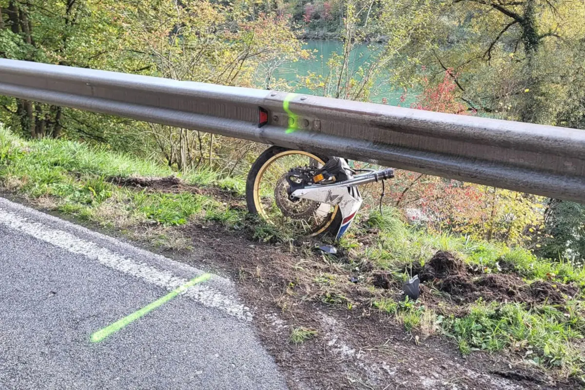 Ein Motorradreifen steckt in einer Leitplanke fest, nahe einer Straße in ländlicher Umgebung mit einem Fluss im Hintergrund.