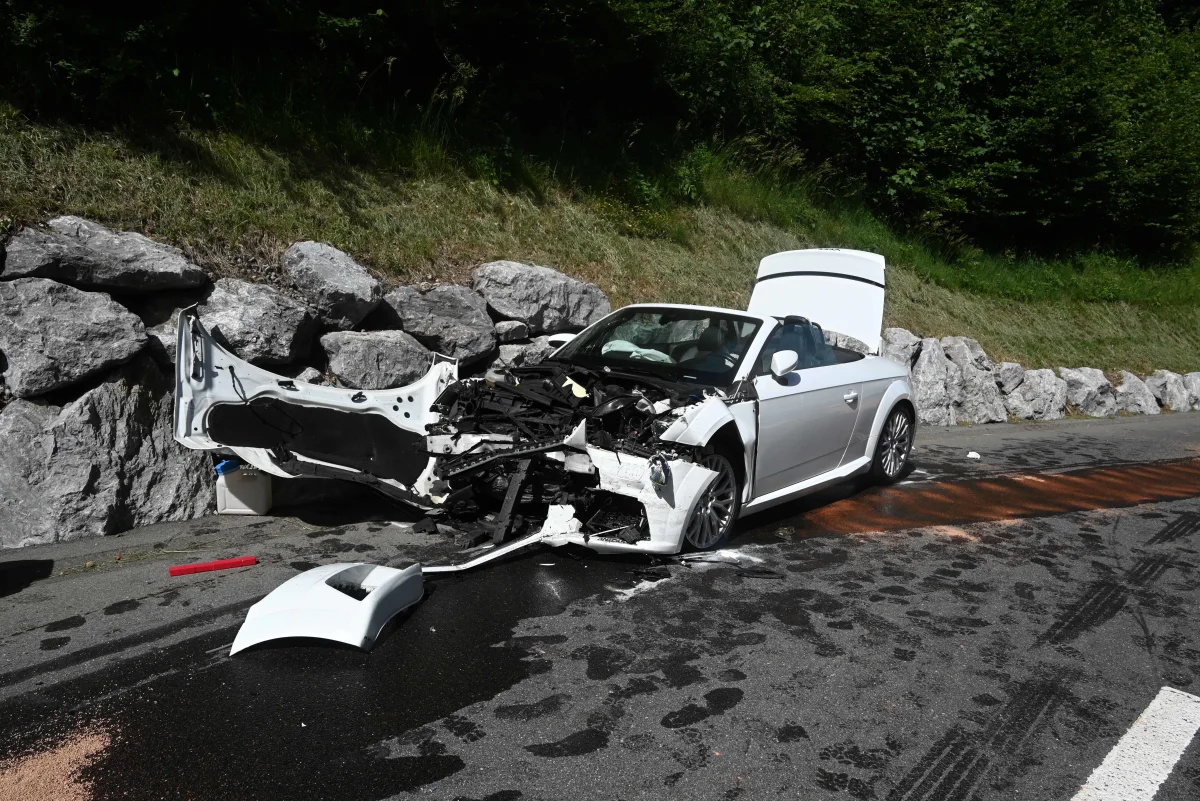 Ein stark beschädigtes weißes Cabriolet steht neben einer Steinmauer. Die Front des Autos ist vollständig zerstört.