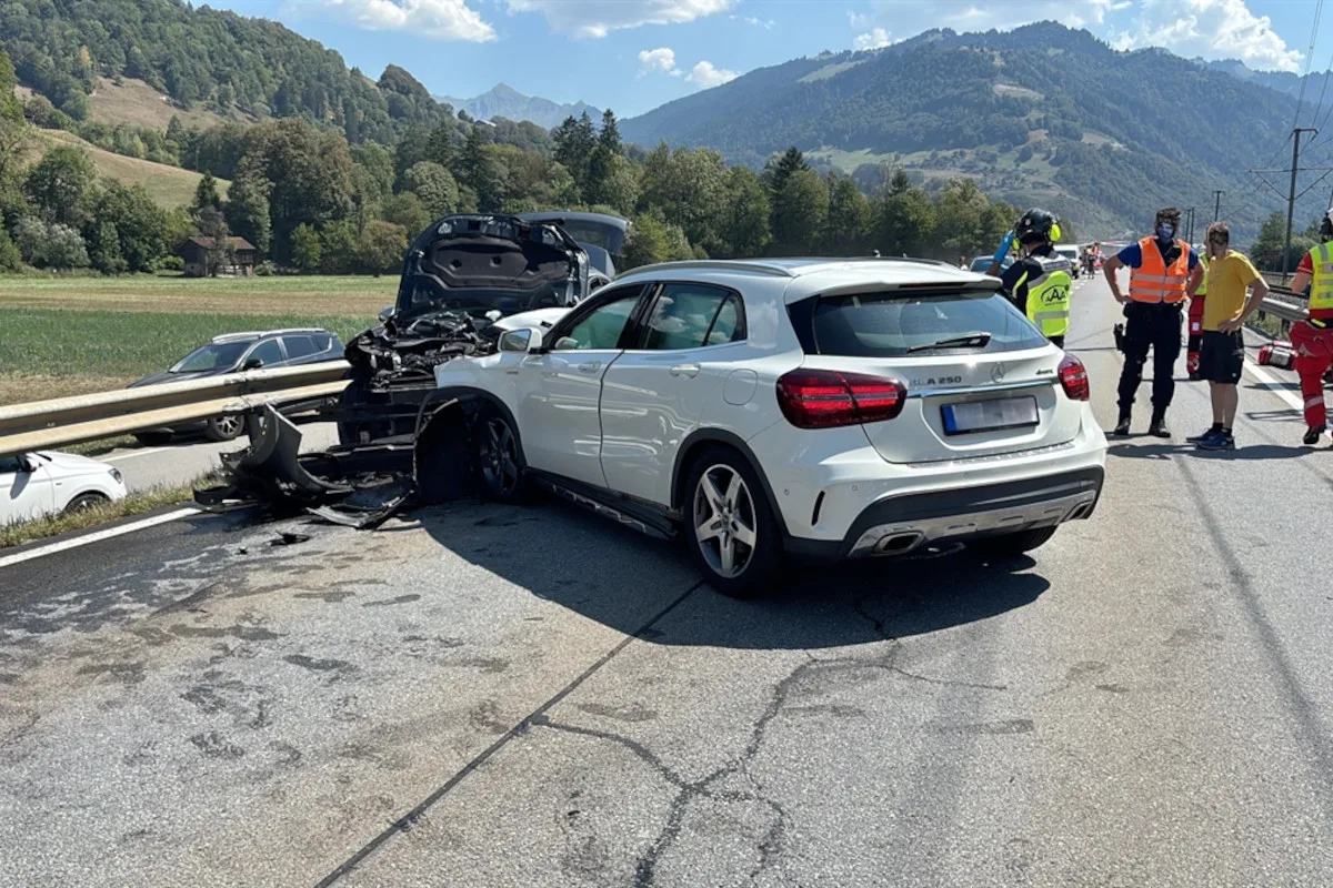 Ein beschädigter weißer Mercedes steht nach einem Unfall auf der Fahrbahn nahe einer Leitplanke. Einsatzkräfte befinden sich in der Nähe.