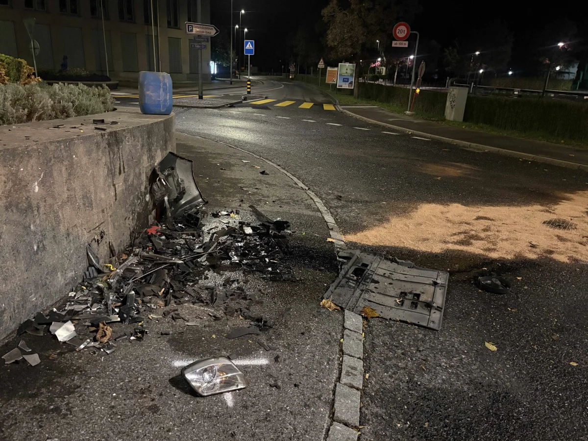 Unfalltrümmer und Flüssigkeitsspuren auf einer Straße bei Nacht neben einer Betonwand in einer städtischen Umgebung.
