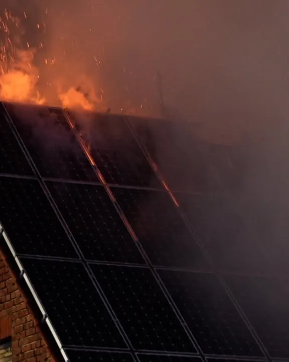 Ein Feuer bricht auf einem Dach mit Solarpanelen aus, Flammen und Rauch sind deutlich sichtbar.