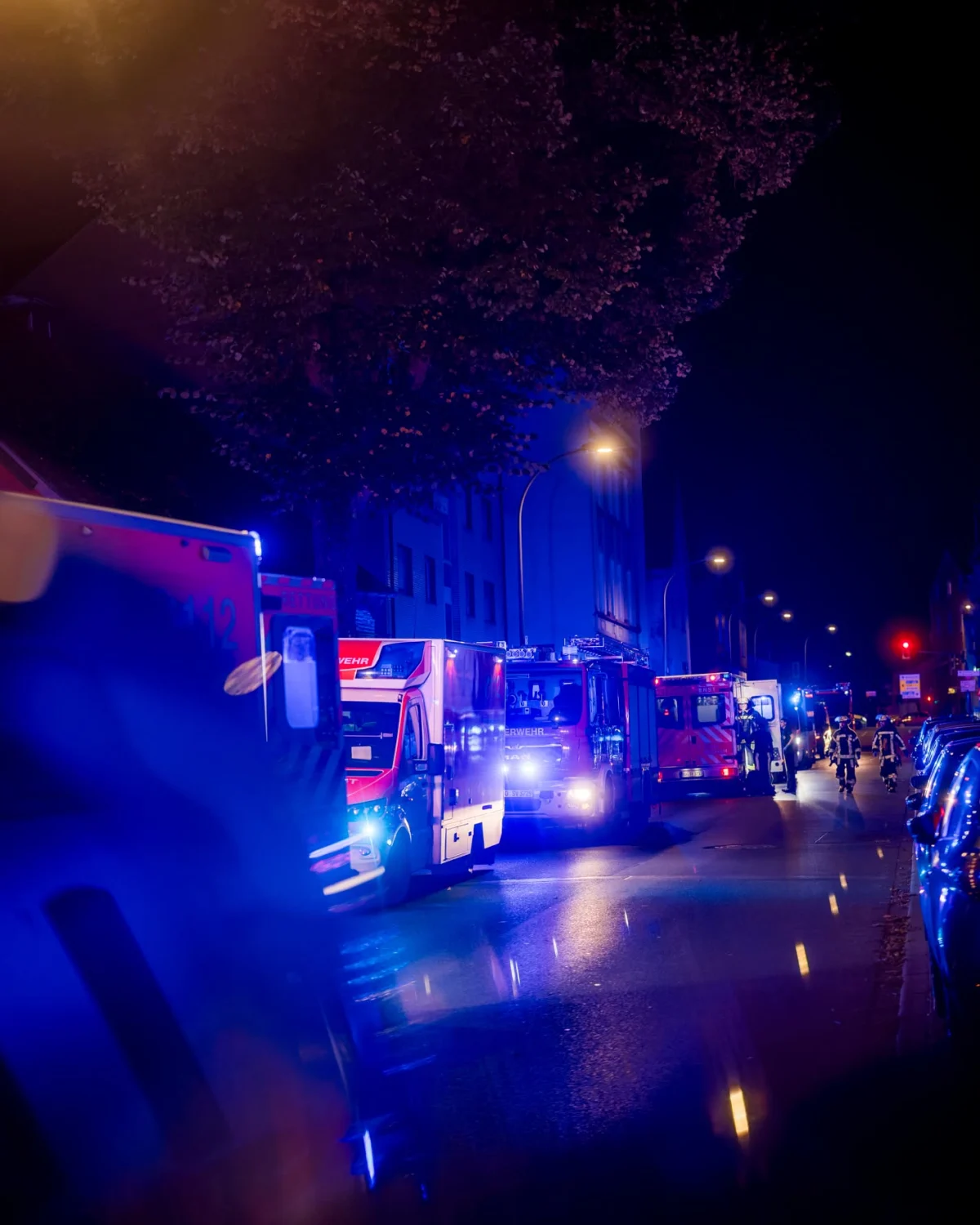 Mehrere Einsatzfahrzeuge mit eingeschaltetem Blaulicht stehen auf einer nächtlichen Straße. Menschen sind zu sehen.