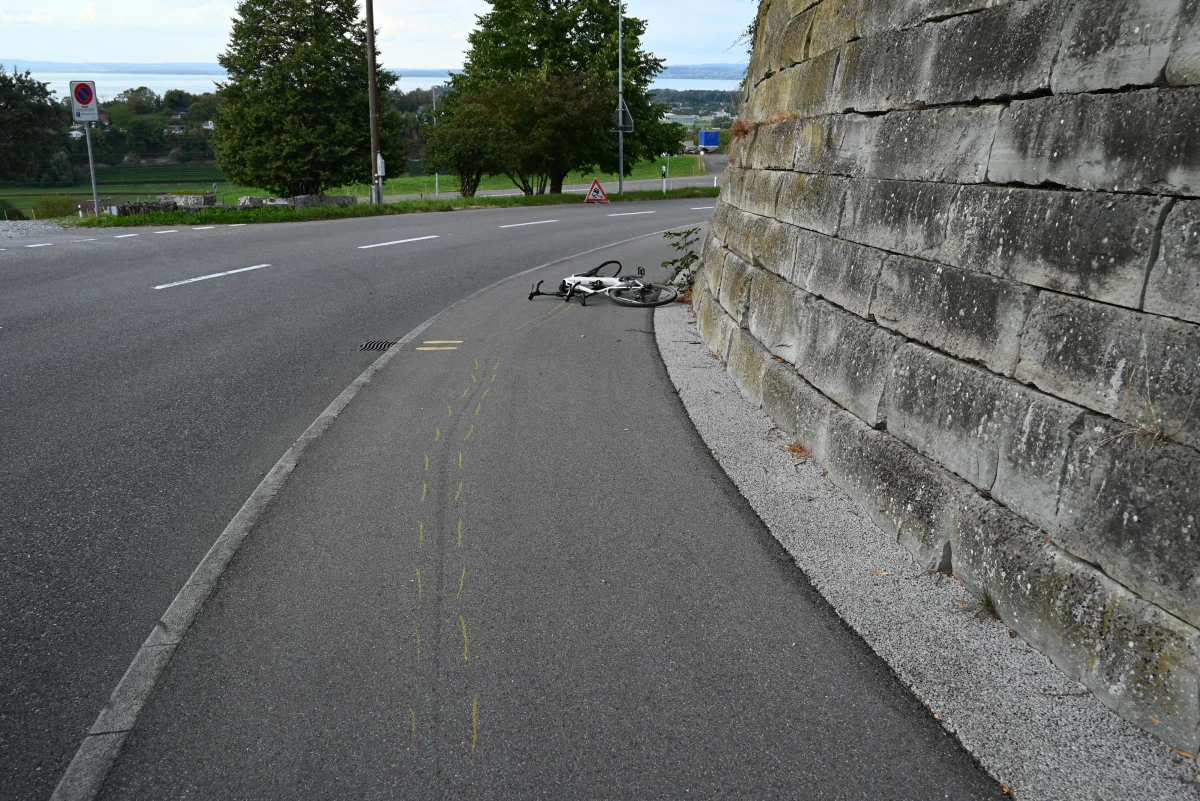 Ein umgestürztes Fahrrad liegt neben einer Mauer auf einem Gehweg. Der Weg ist asphaltiert und leicht geneigt.