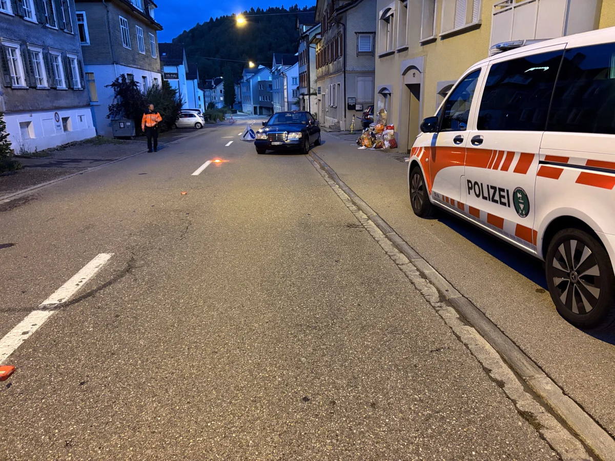 Auf einer nächtlichen Straße stehen ein Polizeifahrzeug und ein Auto. Ein Mann steht in der Nähe des Unfallbereichs.