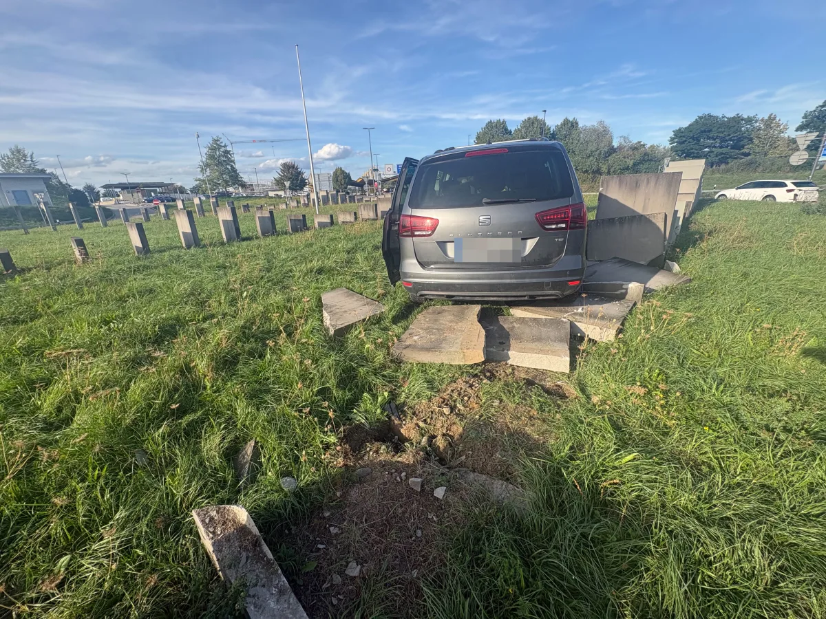 Ein graues Auto steht auf einer Wiese und ist gegen eine Betonmauer gefahren. Die Mauer ist teilweise beschädigt.