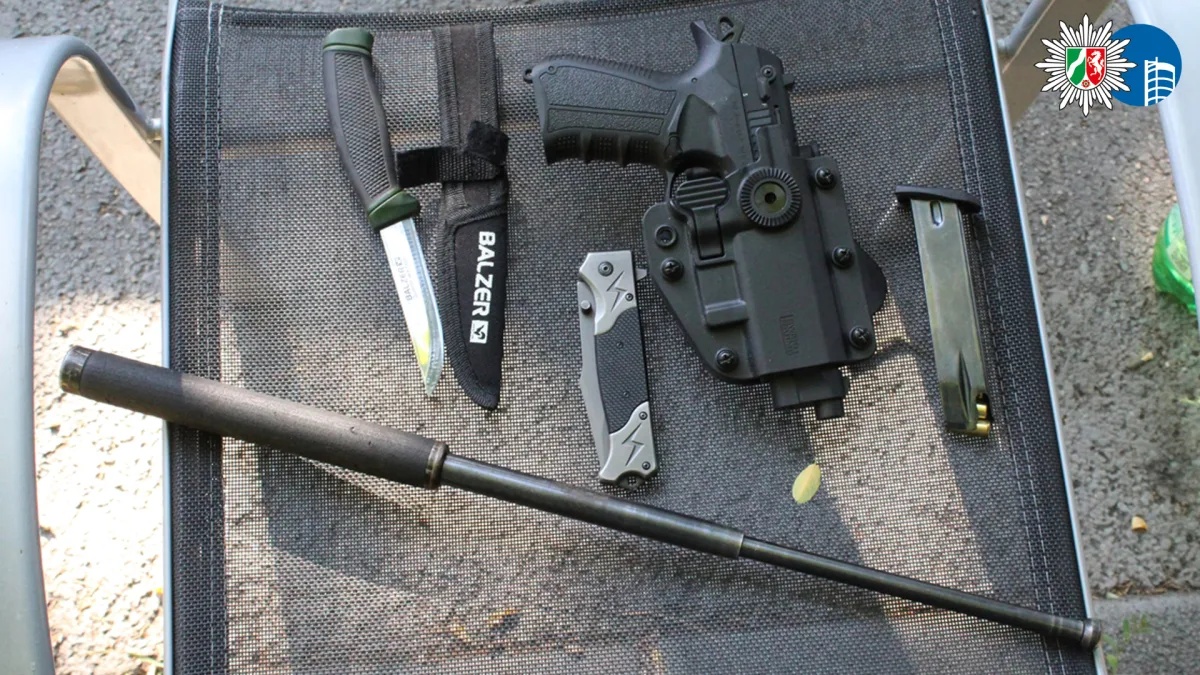 Ein Messer, ein Magazin, eine Schusswaffe und ein Teleskopschlagstock liegen auf einem Stuhl aus Metall.
