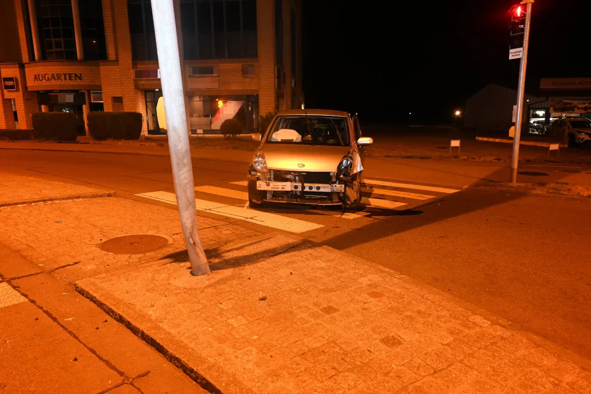 Ein silberfarbener Kleinwagen mit Frontschaden steht nachts auf einem Zebrastreifen. Eine Ampel und ein Gebäude sind im Hintergrund sichtbar.