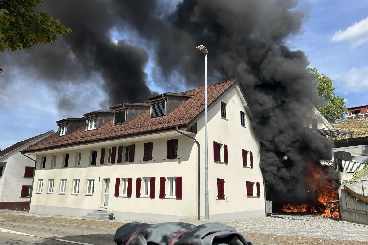 Ein brennendes Gebäude mit dichtem schwarzen Rauch erhebt sich in die Luft. Das Gebäude hat rote Fensterläden.