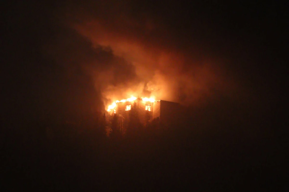 Ein großes Gebäude steht während der Nacht in Flammen. Die Flammen schlagen aus dem Dach und es ist starker Rauch zu sehen.